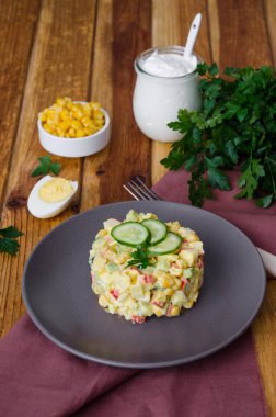 Yengeç çubukları, taze salatalık, mısır ve haşlanmış yumurta ile geleneksel Rus salatası koyu bir tabakta.