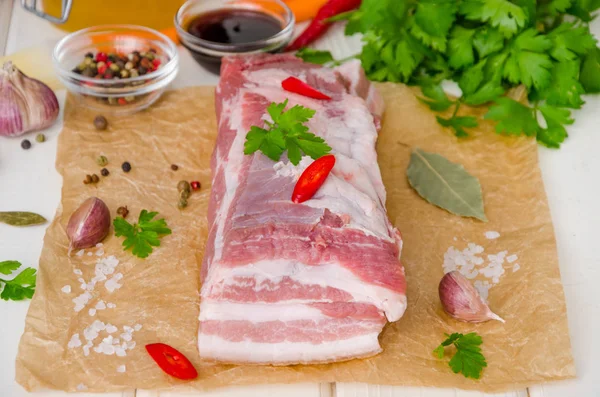 Beyaz ahşap arka plan üzerinde tuz, biber, sarımsak, biber, soya sosu ve bal ile çiğ taze domuz göbeği.