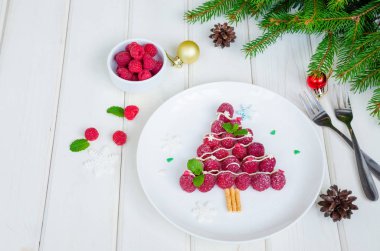 Beyaz çikolata ve pudra şekeri ile beyaz bir tabak üzerinde Ahududu Noel ağacı. Noel yemeği fikri. Sağlıklı tatlı.