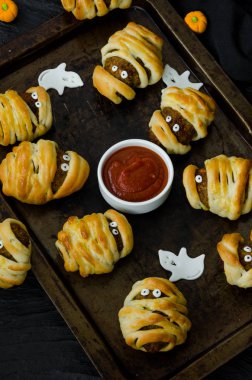 Halloween mumyalar - siyah bir arka plan üzerinde eski bir fırın tepsisine baharatlı domates sosu ile hamur sarılmış köfte. Cadılar Bayramı partisi için fikir.