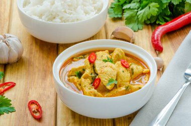 Koyu ahşap arka plan üzerinde bir kase içinde haşlanmış pirinç ile sarımsak ve biber ile sarı köri sosbaharatlı tavuk göğsü.