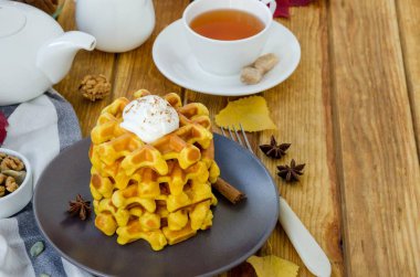 Koyu bir tabakta, karamel soslu ve ahşap arka planda kremalı baharatlı balkabaklı waffle yığını. Kırsal tarzda. Güzel kokulu sonbahar kahvaltısı. Cadılar Bayramı için kahvaltı..