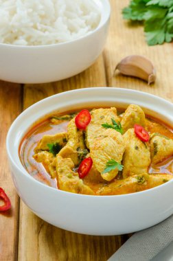 Koyu ahşap arka plan üzerinde bir kase içinde haşlanmış pirinç ile sarımsak ve biber ile sarı köri sosbaharatlı tavuk göğsü.