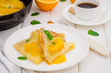 Portakal soslu krep ve beyaz ahşap arka planda bir fincan kahve. Lezzetli ve güzel kokulu kahvaltı..