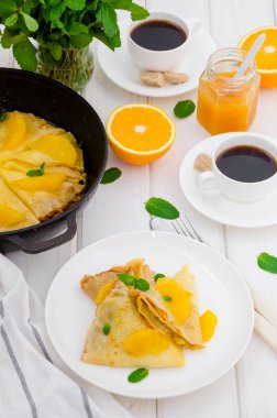 Portakal soslu krep ve beyaz ahşap arka planda bir fincan kahve. Lezzetli ve güzel kokulu kahvaltı..