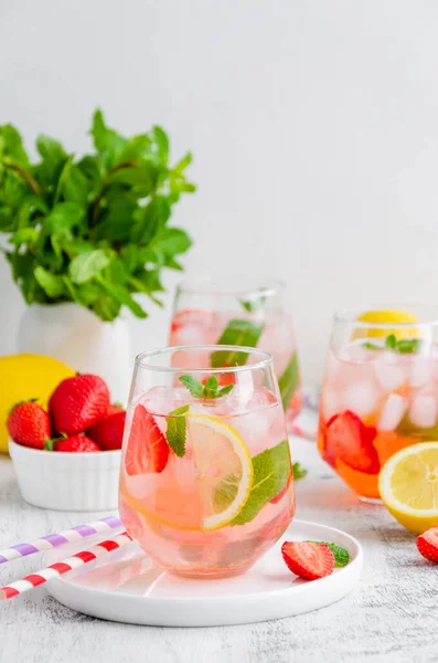 Cold summer drink - strawberry lemonade with mint and ice cubes in glass. Vertical, copy space