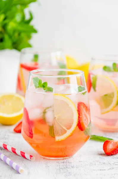 Cold summer drink - strawberry lemonade with mint and ice cubes in glass. Vertical, copy space
