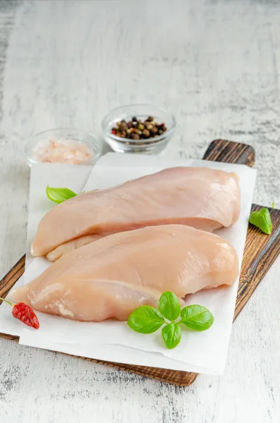 Raw chicken breast on a cutting board with basil and other spices on a light wooden background. Healthy food. Vertical, copy space