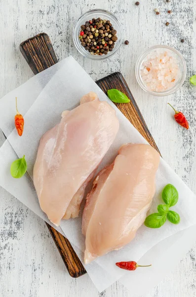 Raw chicken breast on a cutting board with basil and other spices on a light wooden background. Healthy food. Vertical, copy space