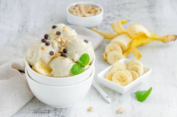 Homemade vegan banana ice cream in a bowl with peanuts and chocolate on a wooden background. Healthy dessert. Horizontal, copy space