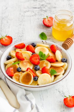 Krep gevreği, taze çilek, yabanmersini ve bal dolu bir kasede mini krep. Moda yemeği. Dikey, boşluğu kopyala