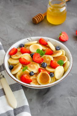 Krep gevreği, taze çilek, yabanmersini ve bal dolu bir kasede mini krep. Moda yemeği. Dikey, boşluğu kopyala