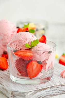 Çilekli dondurma bardakta taze çilek, çikolata damlaları ve açık tahta zemin üzerinde nane şekeri. Dikey, boşluğu kopyala