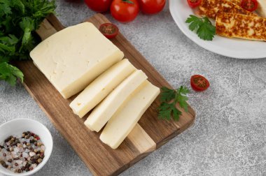 Ahşap bir tahtanın üzerinde beyaz peynir halloumi ve çimento kaplı otlar ve domatesler. Üst görünüm