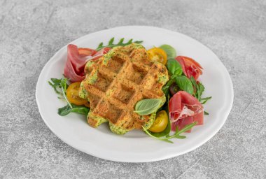 Beyaz tabakta domatesli ıspanaklı waffle, roka ve prosciutto ile bir fincan kahve. Sağlıklı kahvaltı. Üst görünüm.