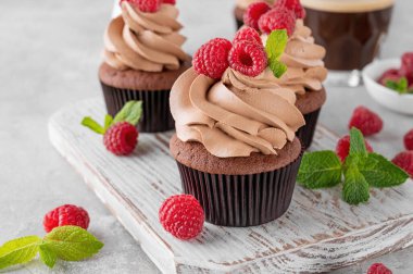 Kremalı çikolatalı kekler taze ahududu ve gri beton arka planda nane yapraklarıyla süslenmiş. Lezzetli bayram tatlısı.