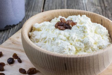 Homemade curd in a wooden bowl with raisins on a old board clipart