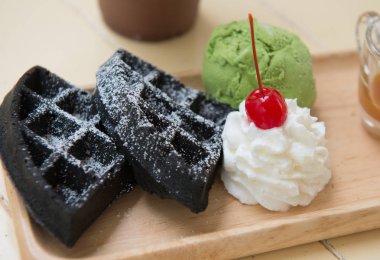 Ahşap çanak içinde kırbaçlanan krem ve şeri ile Kömür waffle ve yeşil çay dondurma yakın