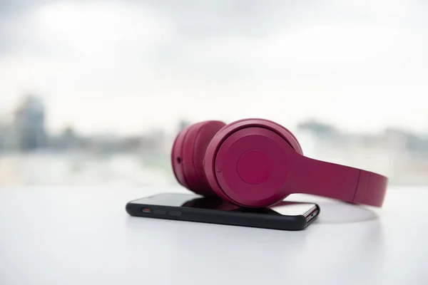 Auriculares inalámbricos rosa y teléfono inteligente en la mesa blanca — Foto de Stock