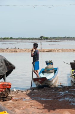 Genç Kamboçyalı adam Tonle Sap gölündeki teknesinde ayağa kalkar.