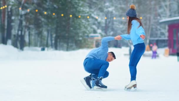 Chica ayuda novio de pie de hielo en pista de patinaje — Vídeo de stock