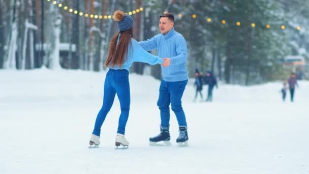 Мужчина и девушка в джинсах и свитерах катаются на коньках взявшись за руки — стоковое видео