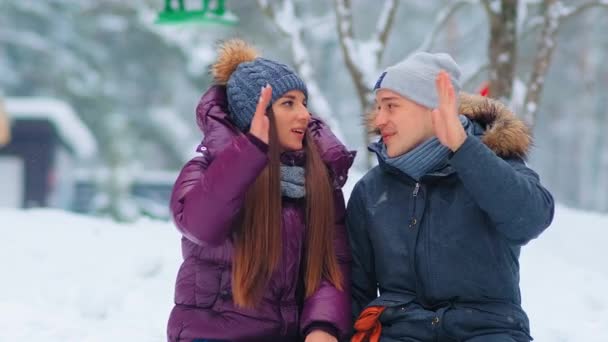 Kalın ceketli pozitif çift, karlı şehir parkında beş veriyor. — Stok video