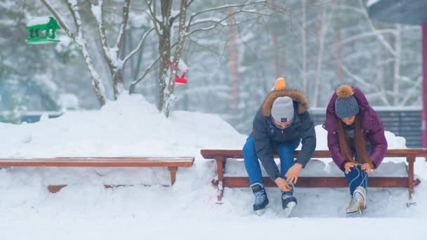 Lady and guy lace skates sitting on bench near open ice rink — Stock Video