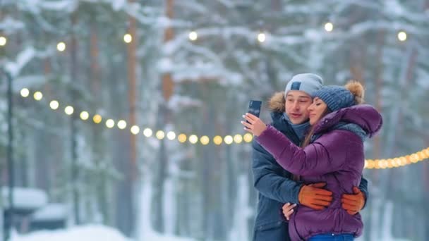 Encantadora pareja hace selfie con teléfono besos en snowy park — Vídeo de stock