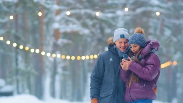 Sıcak ceketli genç çift karlı şehir parkında selfie çekiyor. — Stok video