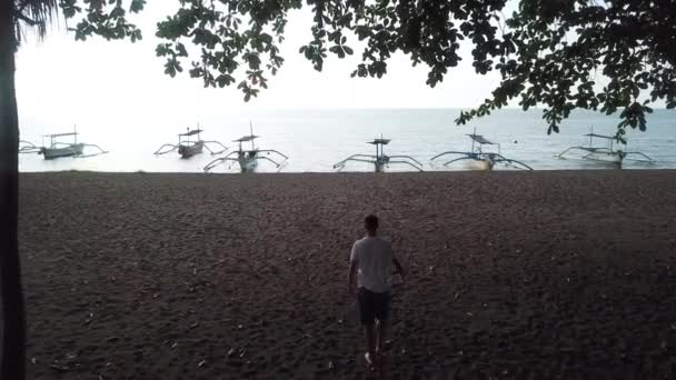 Han går langs stranden og rekker opp hånden. – stockvideo