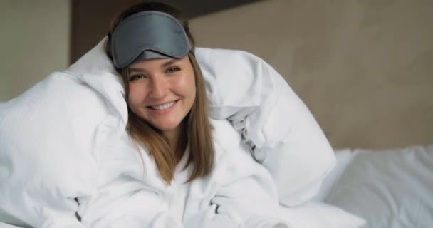 Femme souriante dans le masque de sommeil se trouve sous la couette sur le lit gros plan — Video