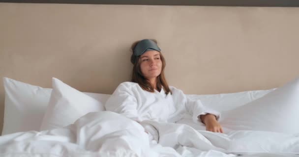 Mulher com máscara de sono e pijama encontra-se na cama confortável — Vídeo de Stock