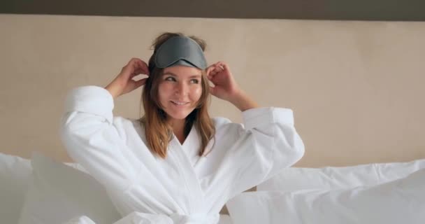Женщина в халате регулирует маску лежащей на удобной кровати — стоковое видео