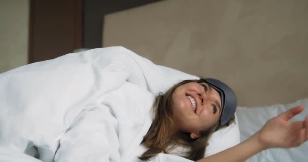 Mujer joven con máscara se encuentra debajo de la manta en la cama cómoda — Vídeo de stock