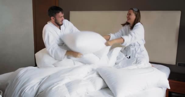 Família jovem tem travesseiro luta jogando na cama confortável — Vídeo de Stock