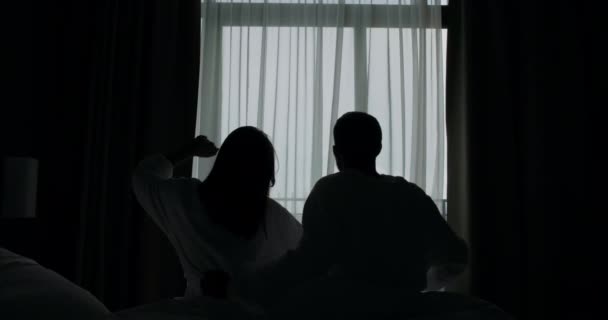 Silhouetten van jong stel dat zich uitstrekt over het bed van het hotel — Stockvideo