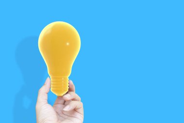 Ampul sarı pastel renk mavi arka plan, fikir ve enerji kavramı üzerinde tutan el.