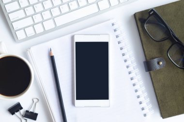 Bilgisayarlı beyaz masa ofisi, akıllı telefon ve bir fincan kahveli diğer iş malzemeleri. Metni kopyalamak için üst görünümü kullan. Desenci çalışma alanı düz masa üzerinde temel elementler yatıyordu.