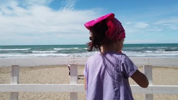 Dziecko dziewczynka jeść lody na plaży bar na wietrze morze z różową bandana — Wideo stockowe