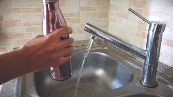 Hand met aluminium milieuvriendelijke fles giet kraanwater uit de gootsteen om plastic gebruik te verminderen — Stockvideo