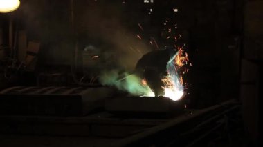 Metalurji üretim. Kaynakçı metal ile çalışır. Yakıcı fly farklı yönlere kıvılcım. Işınları ışık ve duman bulutları.