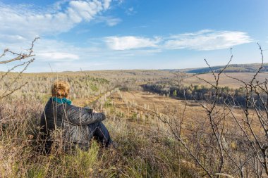 Bir turist sarı çim bir tepenin üstüne oturur. Mevsim değişikliği Batı Sibirya. Giden Sonbaharın sarı renkleri