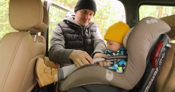 Тато знімає ремінці сидіння і піднімає сина з машини — стокове відео
