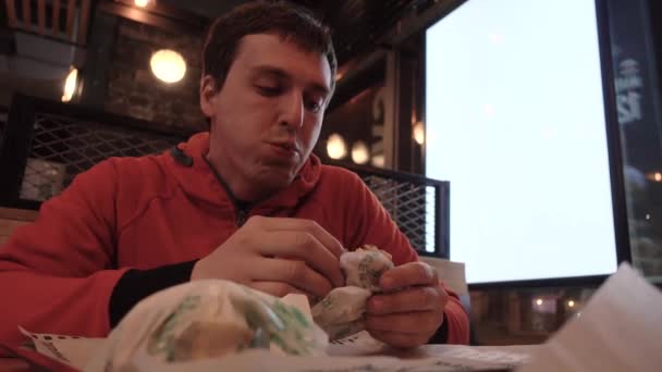 Хлопець кусає великий бургер біля вікна ad scap lightbox — стокове відео