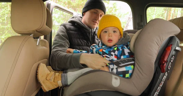 Papá desabrocha correas asiento y levanta hijo hacia fuera coche — Foto de Stock