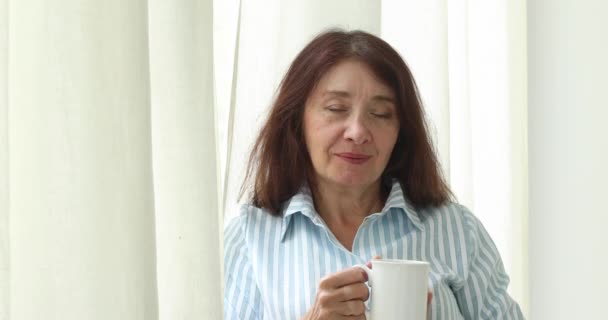 Feliz anciana con taza por ventana en casa — Vídeo de stock