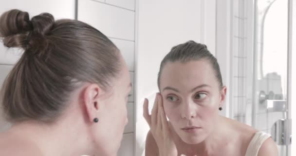 Красива молода жінка перевіряє своє обличчя у дзеркалі — стокове відео