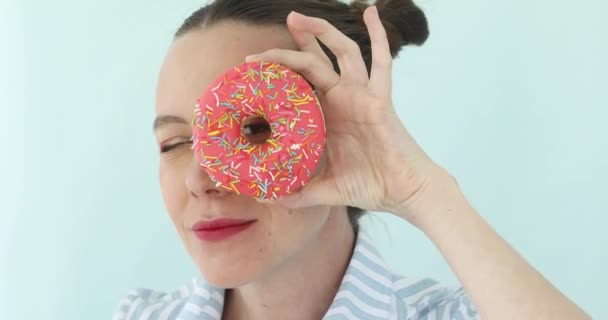 Chica sosteniendo rosado donut mirando a través de agujero — Vídeos de Stock