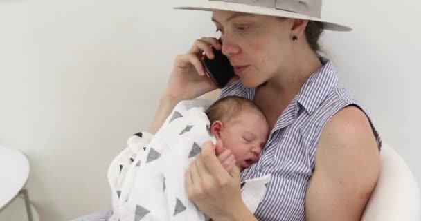 핸드폰에 얘기 하는 그녀의 아기와 함께 젊은 어머니 — 비디오